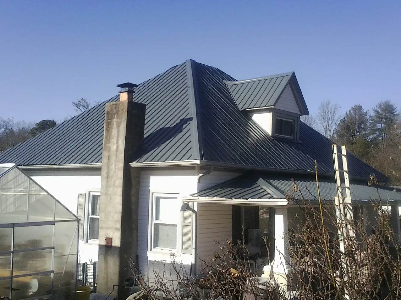 Dark blue standing seam metal roof on a white farmhouse with dormer — Slate & Tile Roof Repair by Roofing Brothers in Green Lake