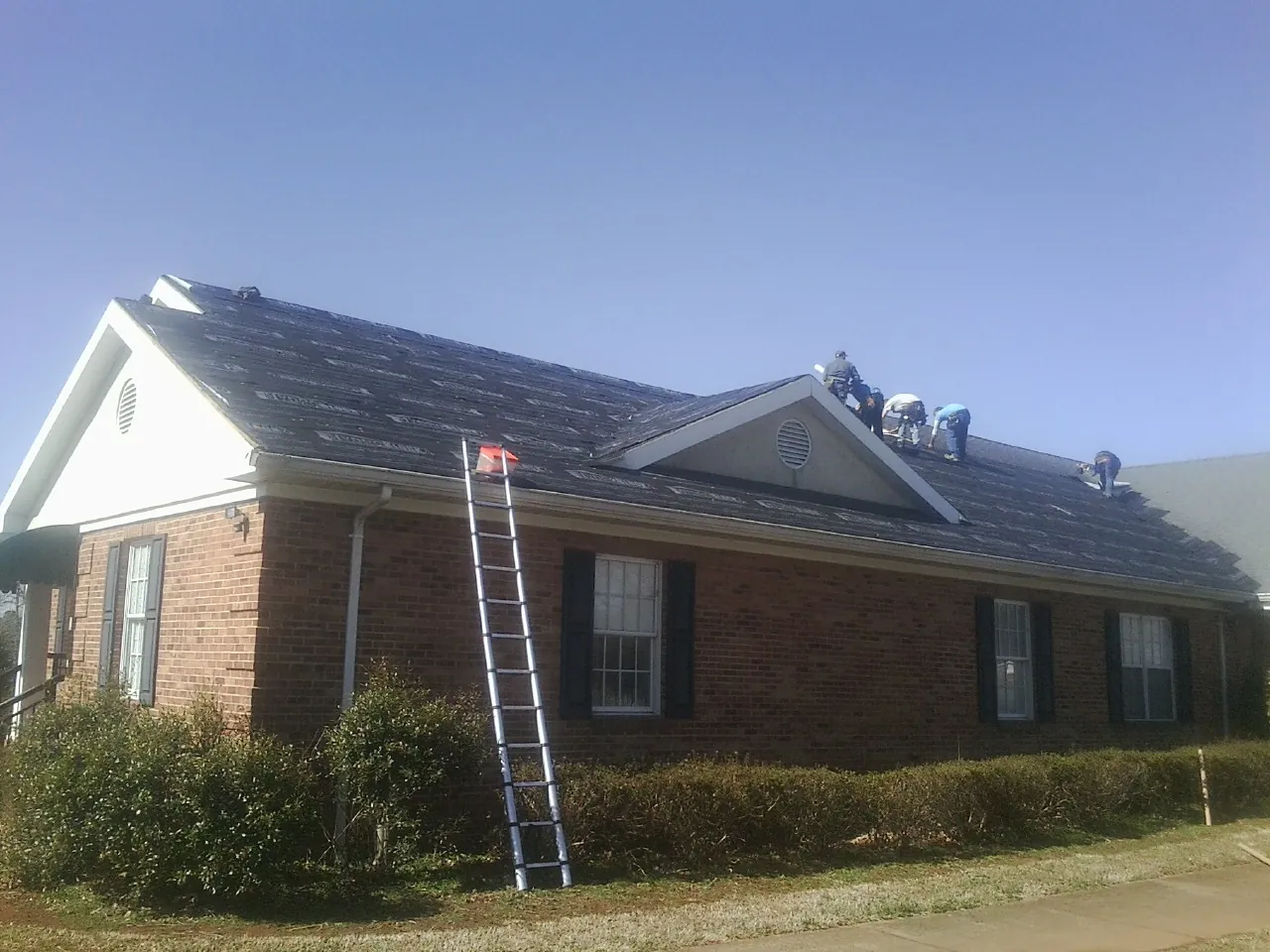 Crew tearing shingles off a brick ranch roof with a ladder set — Metal Roof Repair work by our crew in Green Lake