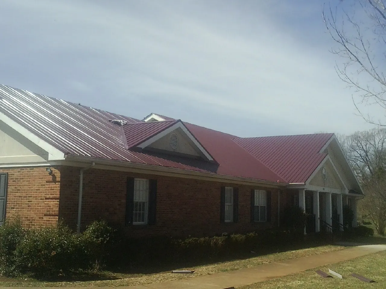 Red metal roof with gabled entries on a long brick building, from a Hail Damage Roof Repair job in Green Lake