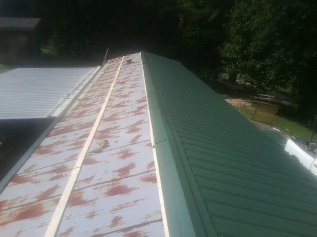 Old rusted panels beside newly installed green metal roofing in Green Lake