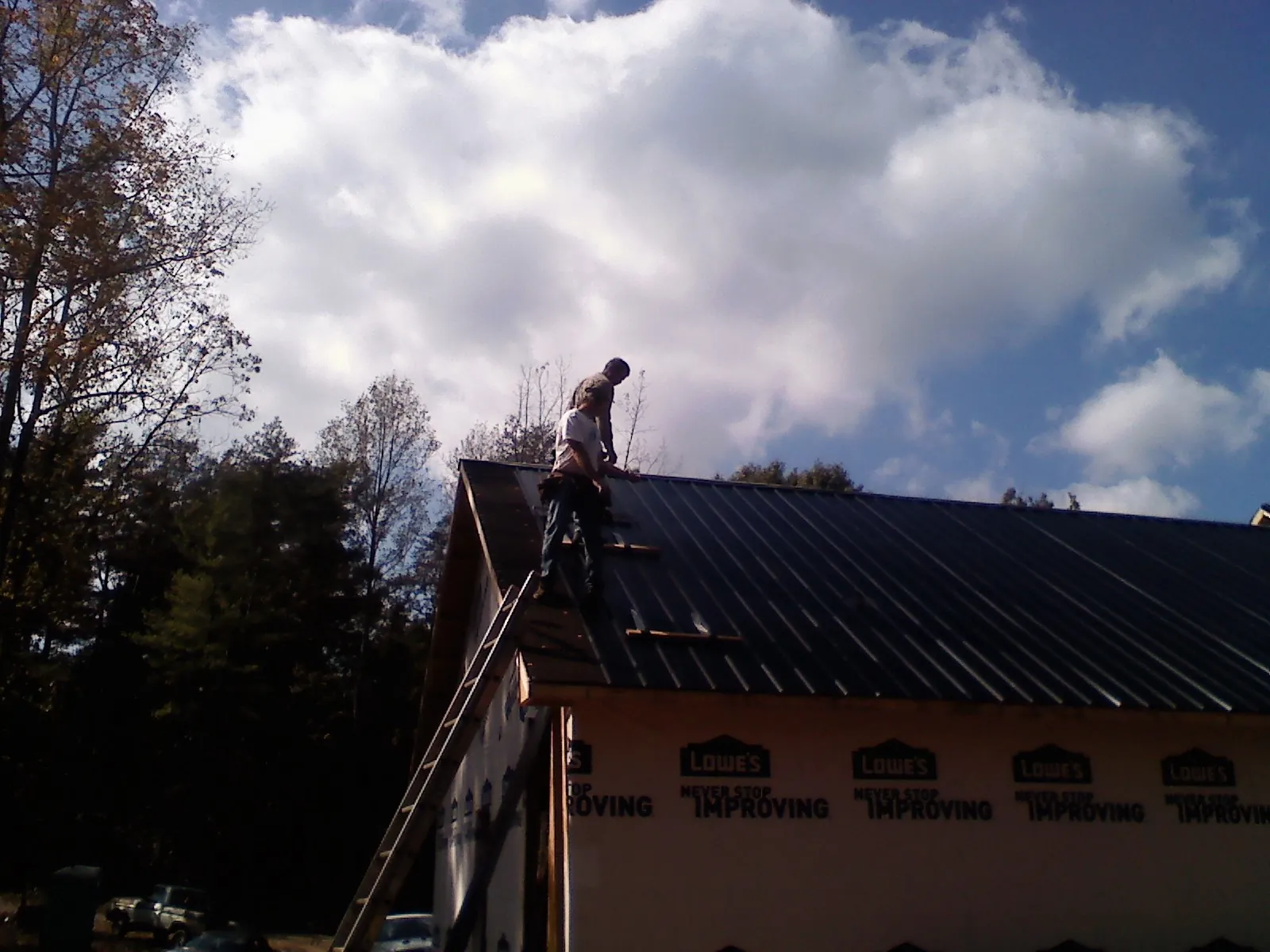 Roofer fastening dark metal panels high against a cloudy sky, from a Roof Inspection job in Green Lake