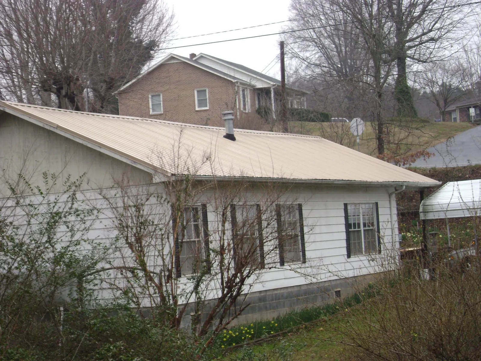 Tan metal roof on a white sided house set into a hillside — Commercial Roofing by Roofing Brothers in Green Lake