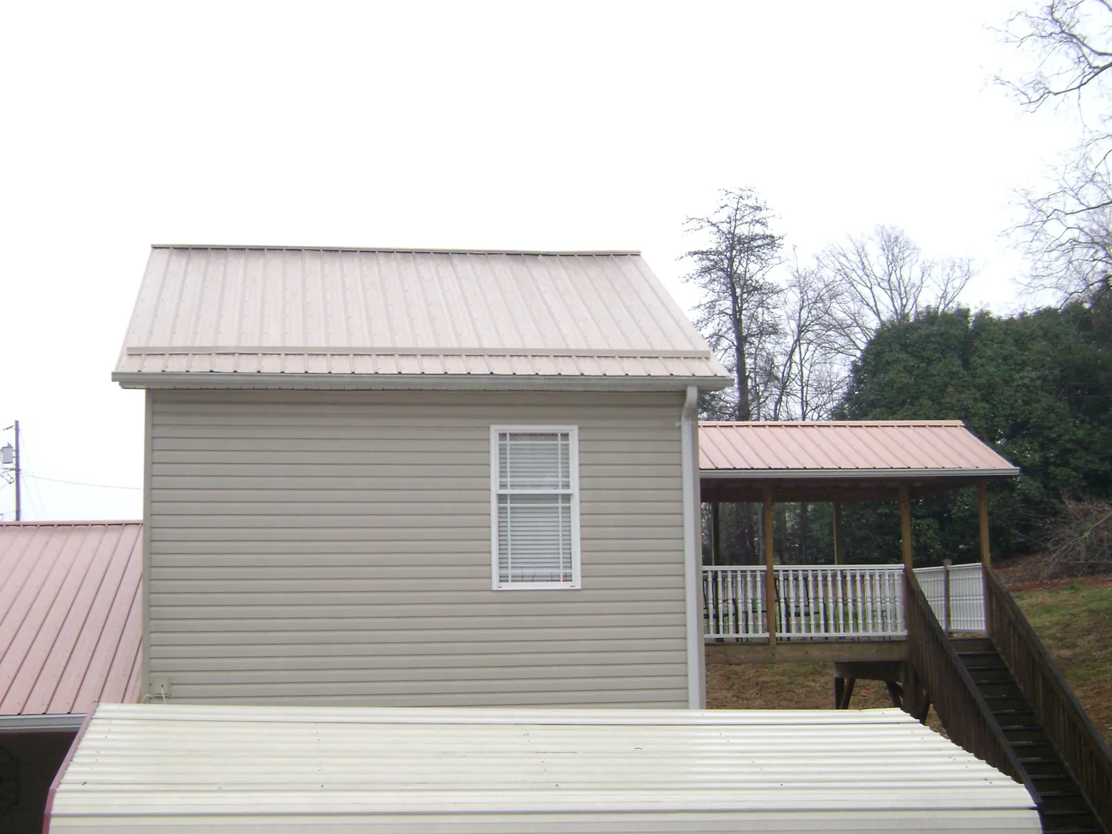 Tan metal roofs on a two story addition and attached porch, from a Roof Replacement job in Green Lake
